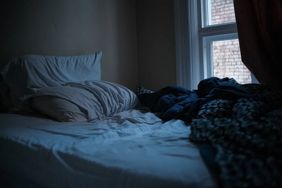 An unmade bed in a dark, quiet bedroom