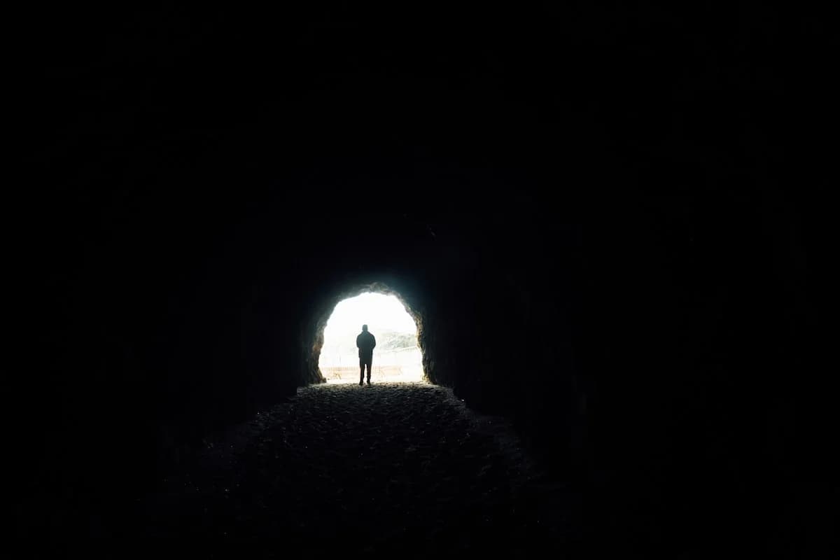 A person standing in a dark tunnel with a light at the end